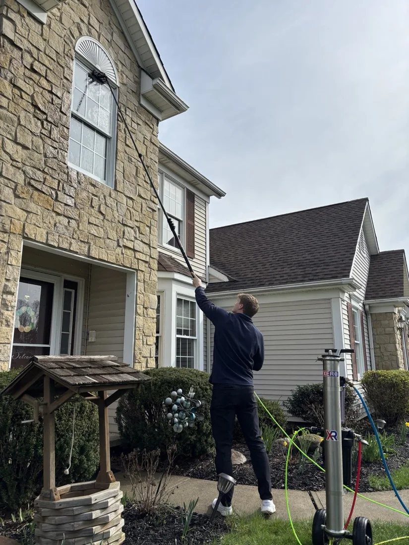 Technician soft washing a home exterior with a water-fed pole