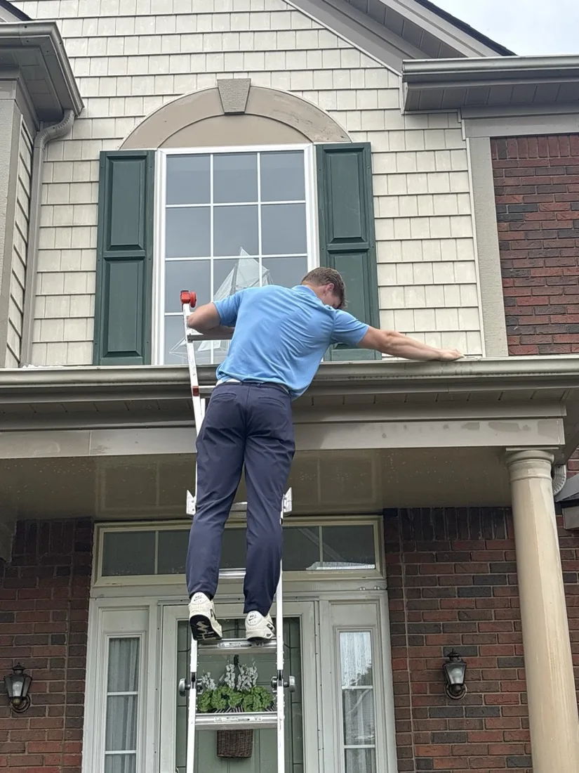 Cleaning a first-floor window under the porch roof