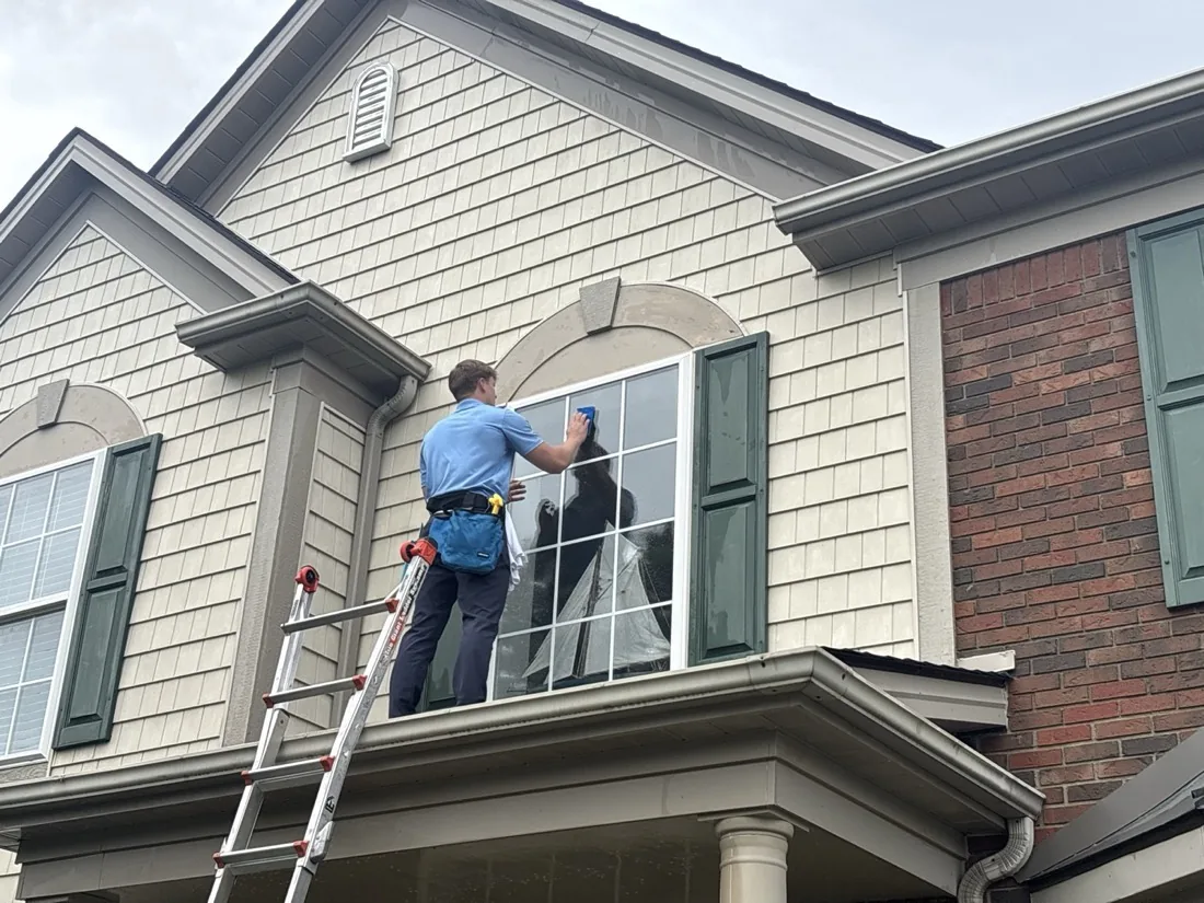 Scrubbing an arched second-floor window with a soaped brush