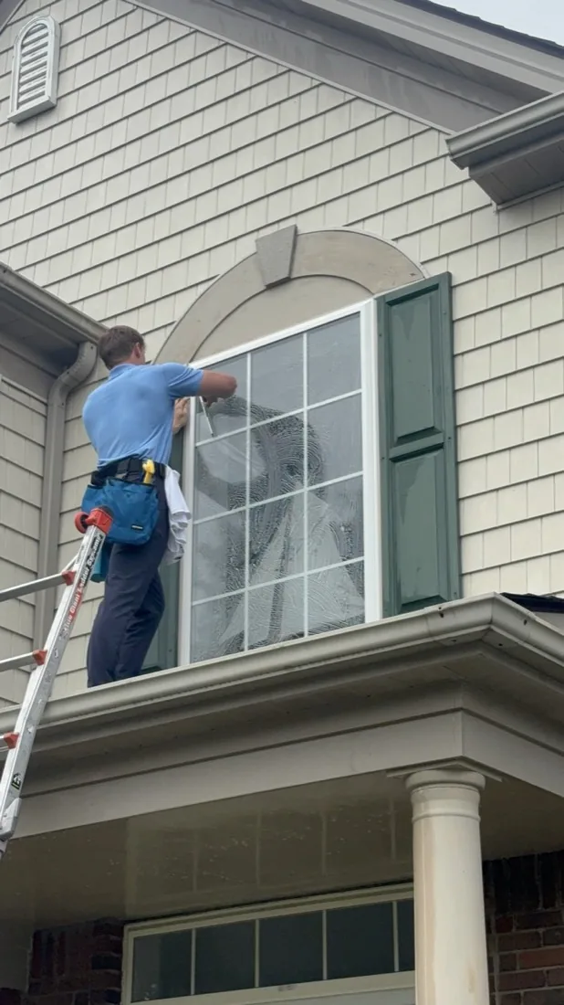 Cleaning the corner pane of an arched window above the porch