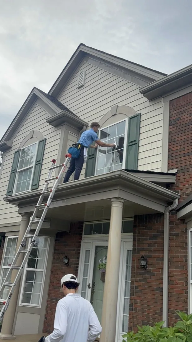 Hand-cleaning exterior window glass on a two-story home